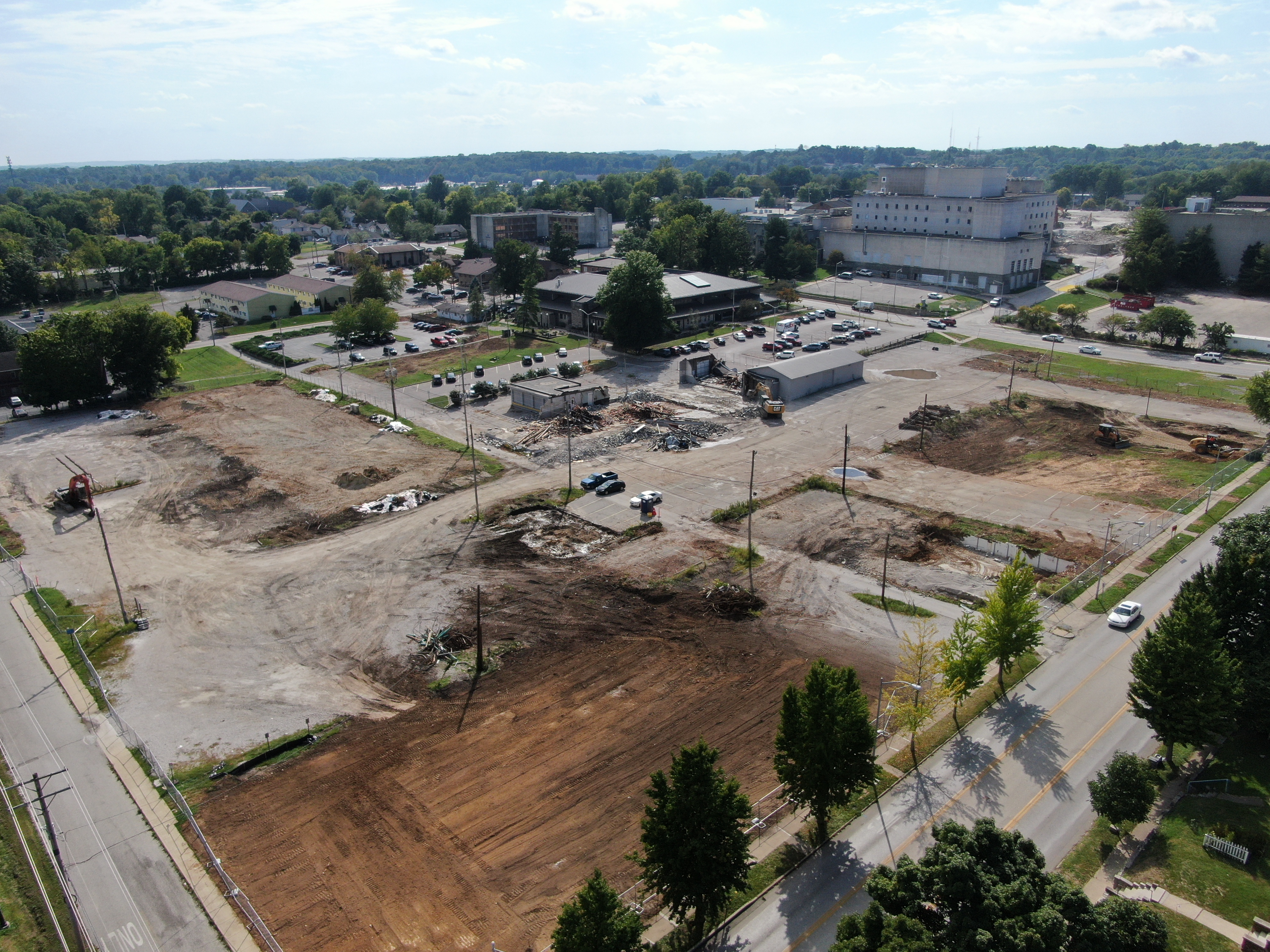 The right photo is looking southwest from the intersection of 2nd and Morton Street, there is a cleared site with exposed earth and the same equipment as the left photo working in the middle ground, the legacy hospital is shown in the background.&nbsp;