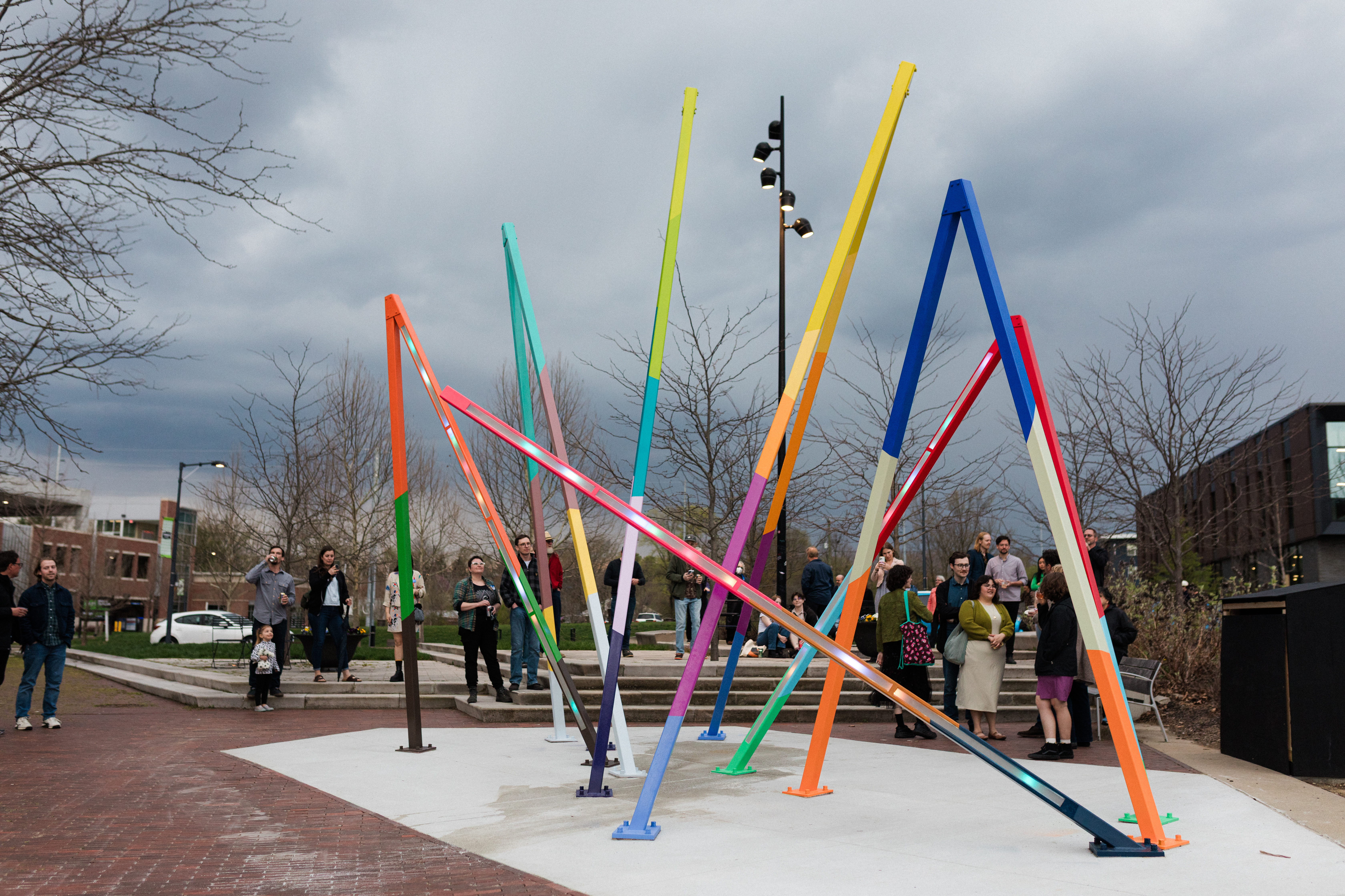 huge colorful light sculpture sticking out of ground with residents viewing it in the early evening